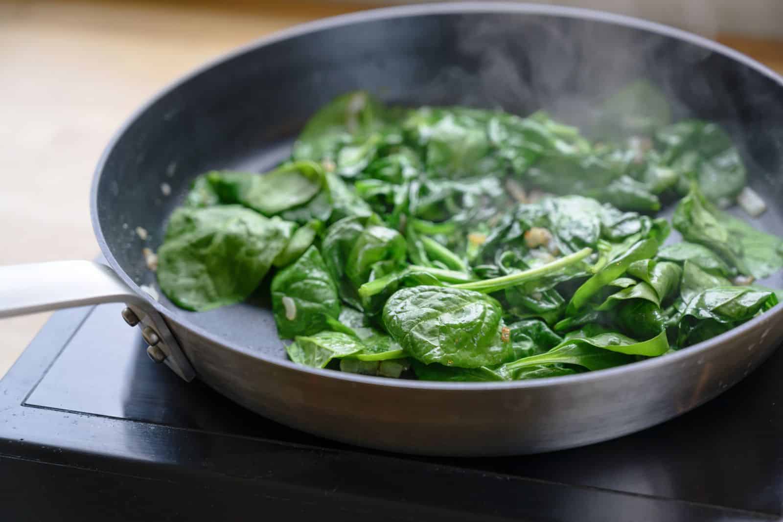 Spinach is being cooked in a pan on a stove.